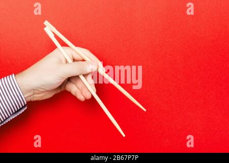 Bacchette di legno sostenuto con maschio mani su sfondo rosso. Pronto per mangiare con i concetti di spazio vuoto. Foto Stock