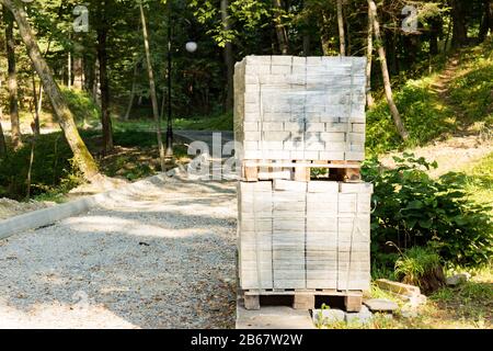 Pile di lastre per pavimentazione in calcestruzzo su pallet in legno. Blocchi per la pavimentazione di un marciapiede nel parco. Foto Stock