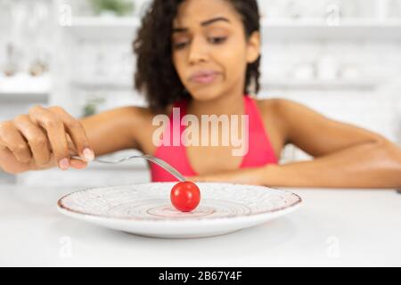 Infelice afro donna che guarda il pomodoro piccolo su un piatto Foto Stock