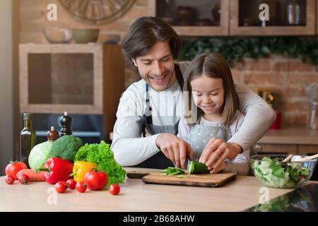 Il padre che si prende cura di lui insegnava a sua figlia a cucinare, tagliando il cetriolo insieme Foto Stock