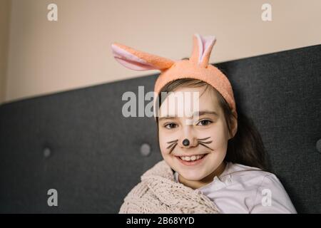 Felice ragazza cute che indossa orecchie bunny arancione. Giovane ragazza sorridente con faccia dipinta come coniglietto per Pasqua che indossa la fascia con le orecchie. Foto Stock