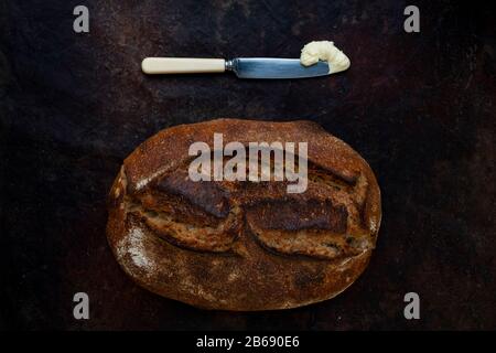 Focaccia di pane appena sfornata in una panetteria artigianale con un coltello e una porzione di burro. Foto Stock