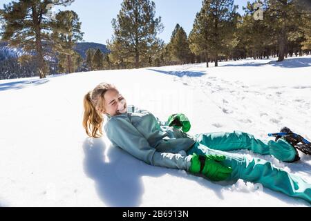 Una ragazza adolescente che indossa scarpe da neve sdraiata sulla neve ridendo Foto Stock