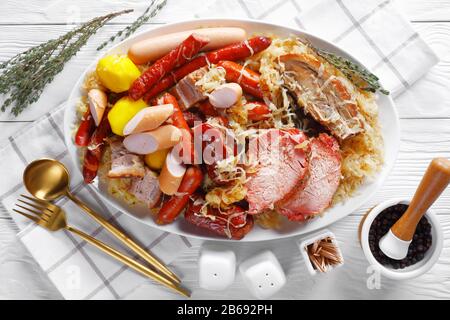 Choucroute garnie cavolo alsaziano acido stufato con salsicce affumicate, lombata di maiale, pancetta cotta con patate in vino bianco con bacche di ginepro di timo su un w Foto Stock