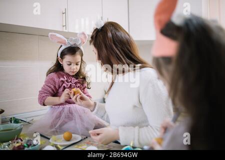 Madre e figlie che decorano le uova di Pasqua. Mamma e sua figlia che attaccano gli adesivi alle uova dipinte per le vacanze di Pasqua nella cucina soleggiata. Foto Stock