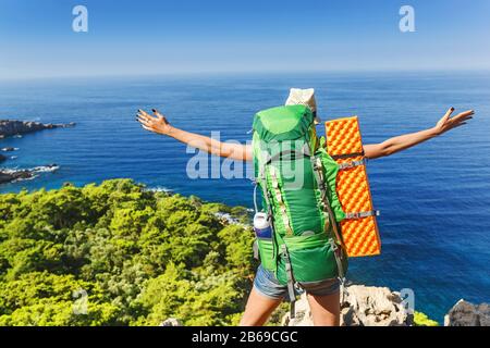 Una giovane donna felice in un viaggio escursionistico con uno zaino sollevato le mani ammirando la colorata vista sul mare. Viaggio attraverso la Via Licia in Turchia Foto Stock