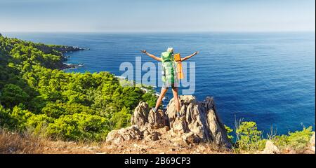 Una giovane donna felice in un viaggio escursionistico con uno zaino sollevato le mani ammirando la colorata vista sul mare. Viaggio attraverso la Via Licia in Turchia Foto Stock