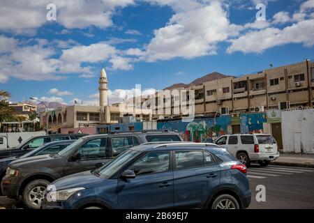 Aqaba, GIORDANIA - 31 GENNAIO 2020: Belle nubi bianche invernali puffy che si muovono in cielo sulla famosa città. Golfo del Mar Rosso, Regno hascemita di Giordania. Vista sulla strada con auto parcheggiate e moschea Foto Stock