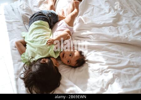 bambino asiatico e sorella piccola che si abbracciano insieme quando si sdraiano sul letto Foto Stock