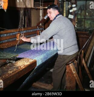 Anni '1960, un uomo che tesseva a mano un panno di mohair su un telaio di legno, Grasmere, Cumbria. Un tessuto o filato di seta, il mohair è realizzato con i lunghi capelli della capra Angora e, come si può vedere, prende bene i coloranti, per produrre capi dai colori vivaci. Foto Stock