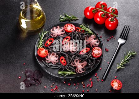 Pasta di pesce nero con gamberi, polpo e cozze su sfondo nero. Cucina mediterranea gourmet. Pasta nera con polpo su un piatto di pietra nera Foto Stock