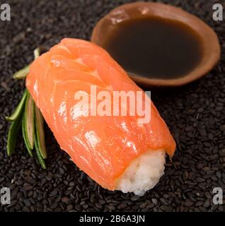Un sushi con salmone su sfondo sesamo nero. Primo piano. Concetto di cibo sano. Fotografia in formato quadrato Foto Stock