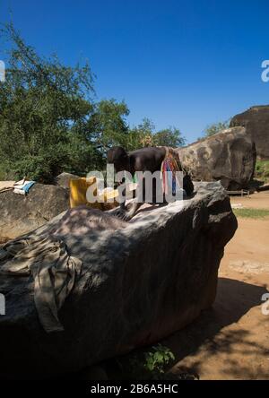 Larim tribù donna macinare grani in un buco nella roccia, Boya Montagne, Imatong, Sudan del sud Foto Stock