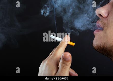 giovane esalerà fumo. danno da fumo sigarette sfondo scuro primo piano. Foto Stock