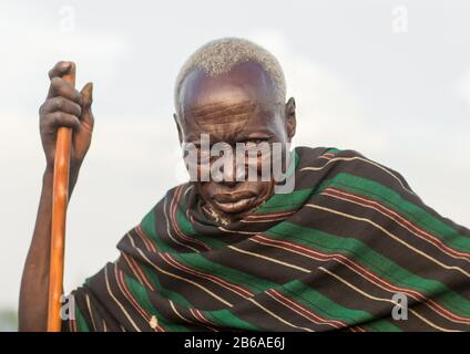 Toposa tribù uomo anziano con un bastone di legno, Stato di Namorunyang, Kapoeta, Sudan del sud Foto Stock