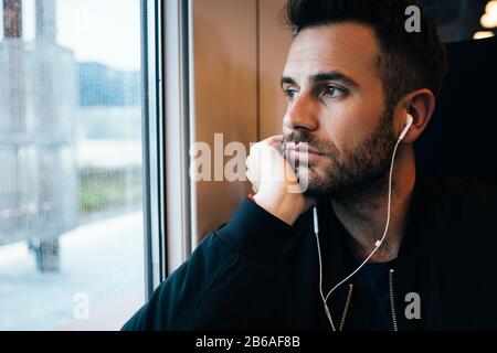 Giovane uomo che viaggia in treno indossando auricolari Foto Stock