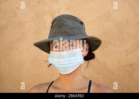 Donna asiatica che indossa una maschera facciale e un cappello Foto Stock