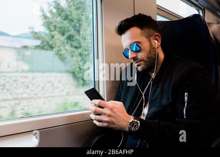 Giovane uomo che viaggia in treno indossando auricolari Foto Stock