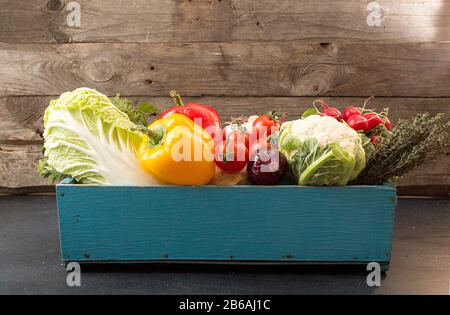 Verdure fresche biologiche fatte in casa in scatola di legno blu su una superficie scura contro vecchio sfondo di legno. Stile rustico. Concetto di cibo sano Foto Stock