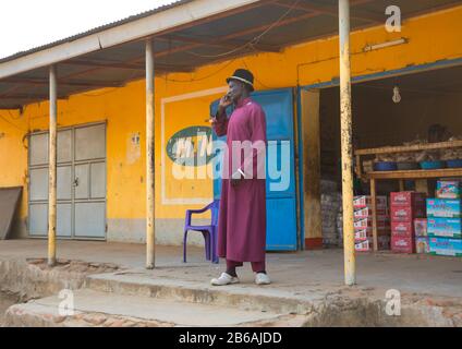Mundari tribù uomo che chiama sul cellulare di fronte a un negozio, Equatoria Centrale, Terekeka, Sudan del Sud Foto Stock