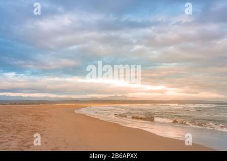 Raggi di golden serata di luce che cade sul Plettenberg Bay spiaggia al tramonto, con montagne in lontananza. Garden Route, Western Cape, Sud Africa Foto Stock