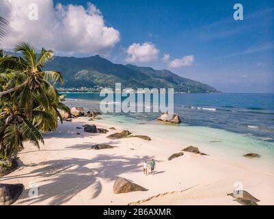 Isole tropicali delle Seychelles, Praslins Island Seychelles con coppie a piedi sulla spiaggia tropicale con palme Foto Stock