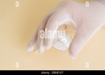 Mano in un guanto bianco che tiene una moneta d'argento bitcoin. Speranza di crescita del capitale Foto Stock