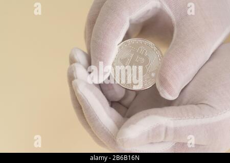 Le mani nei guanti bianchi tengono con attenzione una moneta bitcoin. Speranza di crescita del capitale Foto Stock