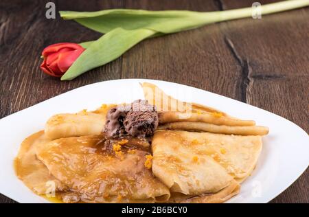 Pancake con salsa dolce e gelato al cioccolato su un piatto bianco. Tulipano fiore sullo sfondo. Foto Stock