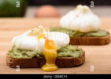 Perdite di tuorlo in camicia. Panini con uovo in camicia e pasta di avocado su pane di cereali. Stile di vita sano. Foto Stock