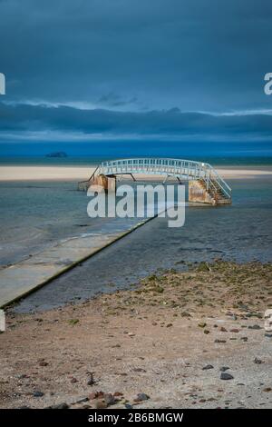 Ponte pubblico sulla spiaggia di Belhaven, vicino a Dunbar, Scozia. Passerella al ponte che è parzialmente tagliato da alta marea. Vivaci colori blu e giallo Foto Stock