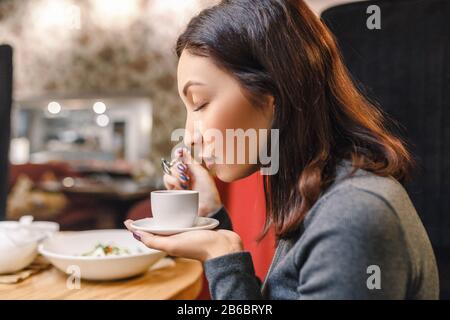Giovane donna orientale che beve un forte aroma di caffè in un caffè Foto Stock