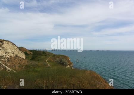 Riva e il ponte Crimea attraverso lo stretto di Kerch. Attrezzatura da pesca vicino alla riva Foto Stock