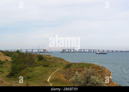 Arco di metallo del ponte Crimea sopra la fairway per il passaggio di navi attraverso lo stretto di Kerch. Vista dalla città di Kerch. Primavera nuvoloso d Foto Stock