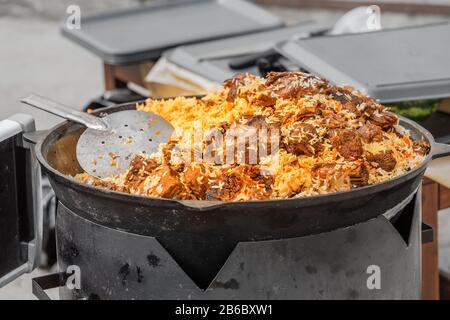 Gustosa Uzbek pilaf in un calderone sul fuoco in aria aperta a street food festival Foto Stock
