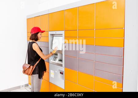 Cliente donna che utilizza una macchina o un armadietto automatico self-service per ricevere un pacco o per depositare il bagaglio per il deposito Foto Stock