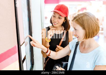 Due amici donna che utilizzano una macchina self-service automatizzata con grande schermo touch digitale. Concetto di tecnologia moderna Foto Stock