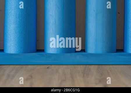 Fusto in schiuma rigida blu su pavimento in legno di quercia con pareti in mattoni bianchi sullo sfondo. Pilates Roll per esercizi di equilibrio e stabilità. Vista frontale, primo piano. Foto Stock