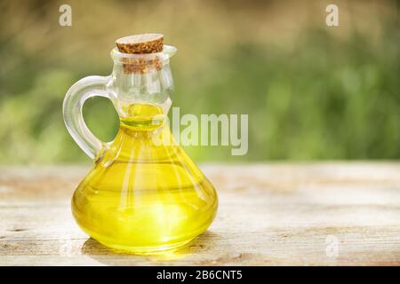 Bottiglia di vetro piena di olio vegetale dorato su un tavolo di legno su uno sfondo verde sfocato. Mock in su per l'olio di insalata o grasso vegetale Foto Stock