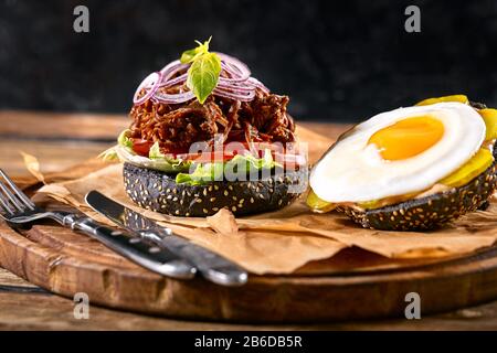 Delizioso hamburger nero piccante con peperoncino e bicchiere di birra su tagliere a tavola di legno bianco. Foto Stock