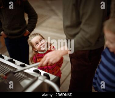 Vista di una bambina sorridente mentre un uomo prepara il barbecue. Foto Stock