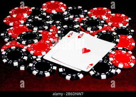 Un paio di assi rossi, diamanti e cuori, su una pila o chip di poker di argilla rossa e nera. Stanza per la copia in basso a sinistra dell'immagine sul feltro rosso ta Foto Stock