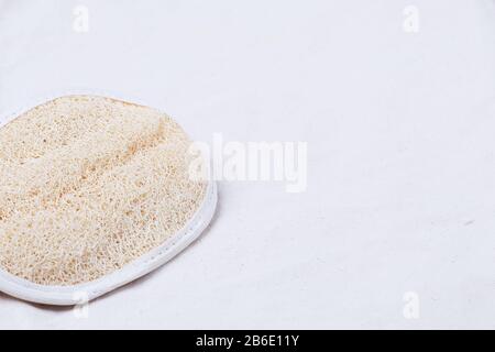 Un guanto in spugna per massaggio luffa o luffah per esfoliazione della pelle su un tessuto di cotone organico beige con spazio per le copie Foto Stock