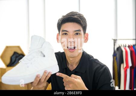 Social media influencer che rivede la moda scarpe. Sorridente giovane uomo che vlogging circa la scarpa sportiva degli uomini e filmarsi a casa su una videocamera. Foto Stock