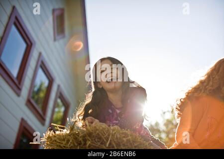 Ridendo giovane ragazza sdraiata in cima su una balla di fieno fuori al sole. Foto Stock