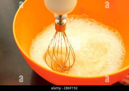 Mescolare le uova nel recipiente arancione con il frullatore Foto Stock