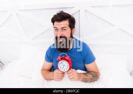 Inizio di giorno impressionante. Svegliati ogni mattina presto. Benefici di salute di aumento presto. Svegliarsi presto dà più tempo. Hippster bearded uomo a letto con sveglia. È ora di svegliarsi. Abitudini sane. Foto Stock