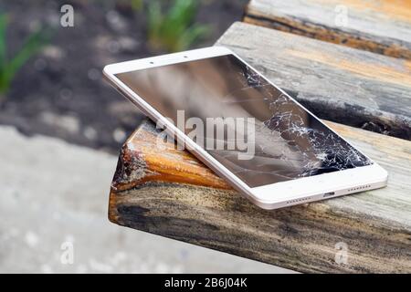 Lo smartphone con schermo rotto si trova sul banco di legno. Messa a fuoco selettiva Foto Stock