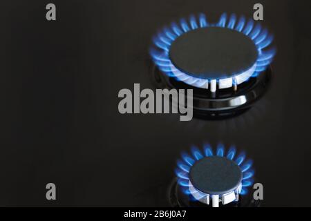 Due bruciatori di gas stanno bruciando con il gas blu sulla stufa scura. Primo piano, messa a fuoco selettiva Foto Stock