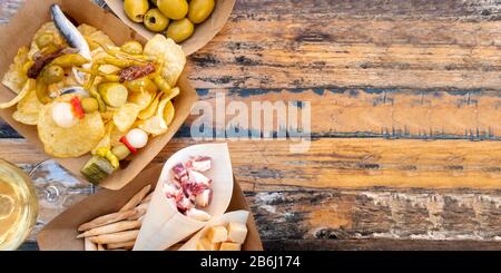 Tapas, pinchos e vino, colpo panoramico in alto su un tavolo di legno. Formaggio, jamon e olive, gildas con peperoni e patatine fritte in un caffè all'aperto Foto Stock